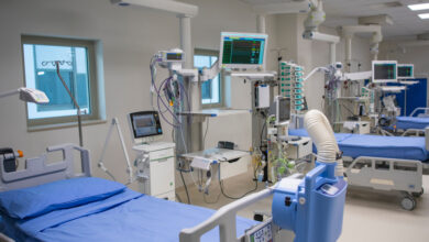 A row of hospital beds with small windows above them surrounded by different types of medical equipment.