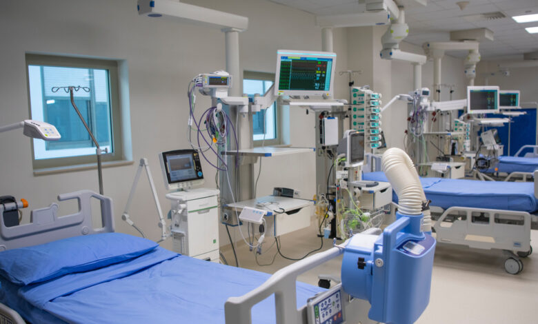 A row of hospital beds with small windows above them surrounded by different types of medical equipment.