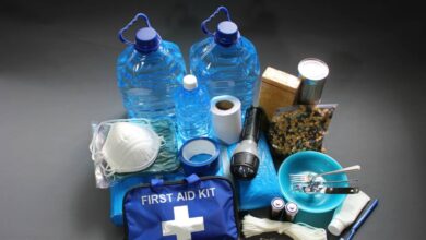 A pile of essentials including gallons of water, a mask, rations, a flashlight, rope, matches, and a first aid kit.