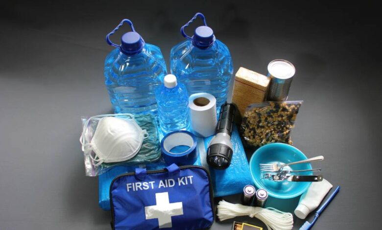 A pile of essentials including gallons of water, a mask, rations, a flashlight, rope, matches, and a first aid kit.