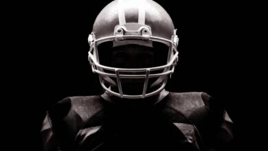 An American football athlete wearing his full team uniform, including his sporting helmet and football jersey.