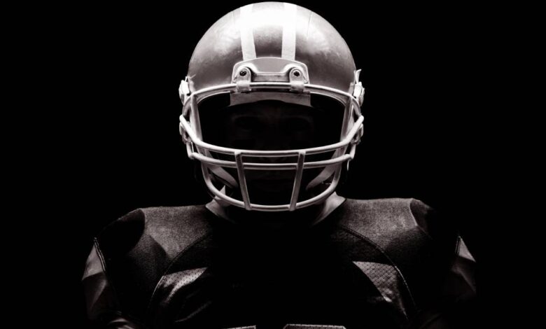 An American football athlete wearing his full team uniform, including his sporting helmet and football jersey.