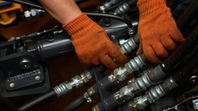 An engineer wearing orange safety gloves as they finesse a section of black hydraulic hose connections.