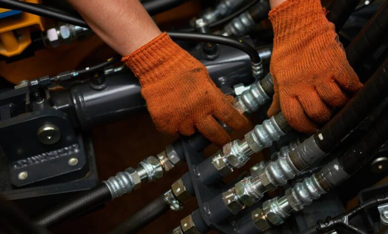 An engineer wearing orange safety gloves as they finesse a section of black hydraulic hose connections.