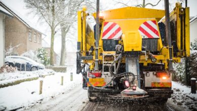 An industrial snow vehicle driving down a residential road. The vehicle is spreading street salt from behind the vehicle.