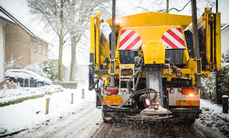 An industrial snow vehicle driving down a residential road. The vehicle is spreading street salt from behind the vehicle.