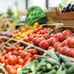 A close-up view shows a display of various fresh vegetables, including tomatoes, zucchini, and potatoes.