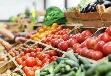 A close-up view shows a display of various fresh vegetables, including tomatoes, zucchini, and potatoes.