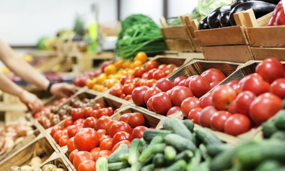 A close-up view shows a display of various fresh vegetables, including tomatoes, zucchini, and potatoes.