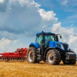 A large, high-performance agricultural tractor pulling a rear-mounted cutting attachment across a grassy field.