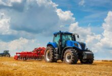 A large, high-performance agricultural tractor pulling a rear-mounted cutting attachment across a grassy field.