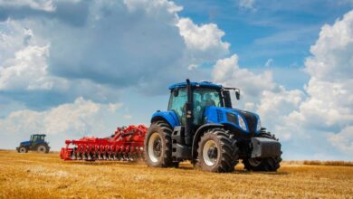 A large, high-performance agricultural tractor pulling a rear-mounted cutting attachment across a grassy field.