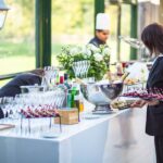 Three catering staff members working around a table beautifully displaying champagne, glasses, and aperitives for a wedding.