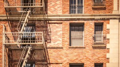 The exterior of a red brick building with a light-colored fire escape. Some of the windows are covered with bars.