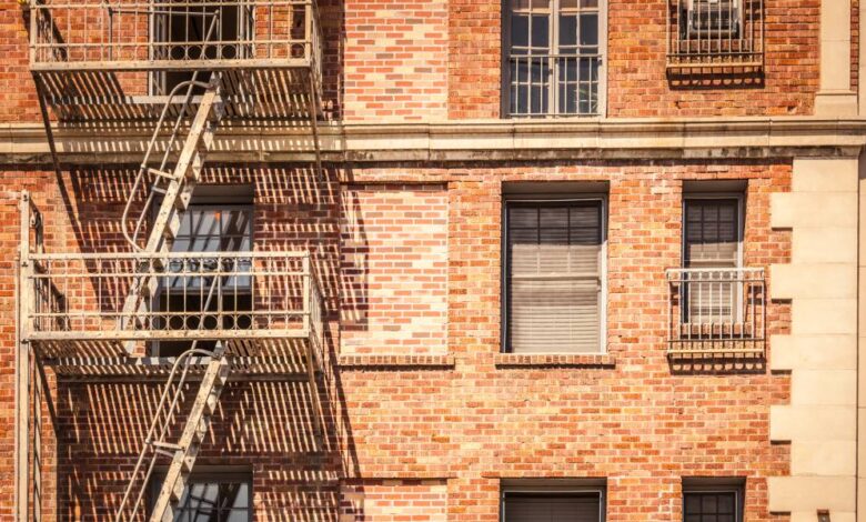 The exterior of a red brick building with a light-colored fire escape. Some of the windows are covered with bars.