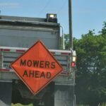 The view of the back of a truck parked on a roadside with an orange hazard sign on it that reads "MOWERS AHEAD."