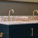 A modern bathroom vanity featuring updated gold hardware with matching faucets and cabinet door handles.