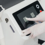 A person wearing white latex gloves is pushing an icon on a screen for a piece of medical equipment.