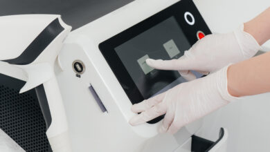 A person wearing white latex gloves is pushing an icon on a screen for a piece of medical equipment.