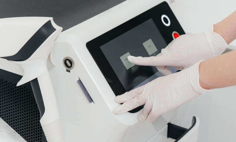 A person wearing white latex gloves is pushing an icon on a screen for a piece of medical equipment.