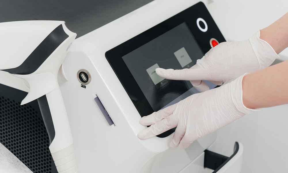A person wearing white latex gloves is pushing an icon on a screen for a piece of medical equipment.