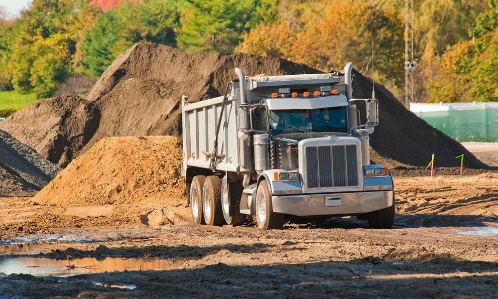 A black and gray dump truck sits on a muddy worksite. A large pile of dirt sits behind the truck.