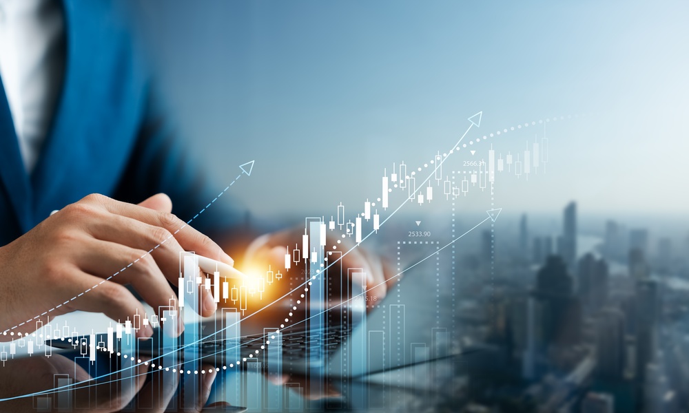 A person in a blue suit sitting at a table using a laptop with images representing financial growth superimposed on top.