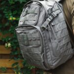 A focus shot of a person wearing a grey MOLLE backpack, a military green t-shirt, and camo pants.