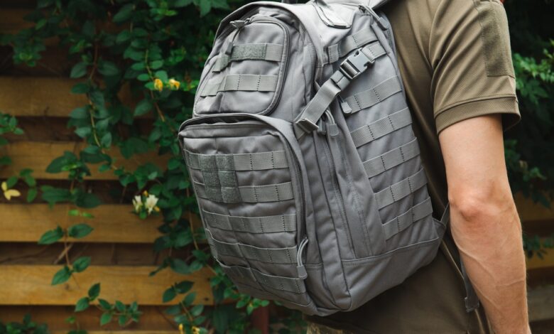 A focus shot of a person wearing a grey MOLLE backpack, a military green t-shirt, and camo pants.