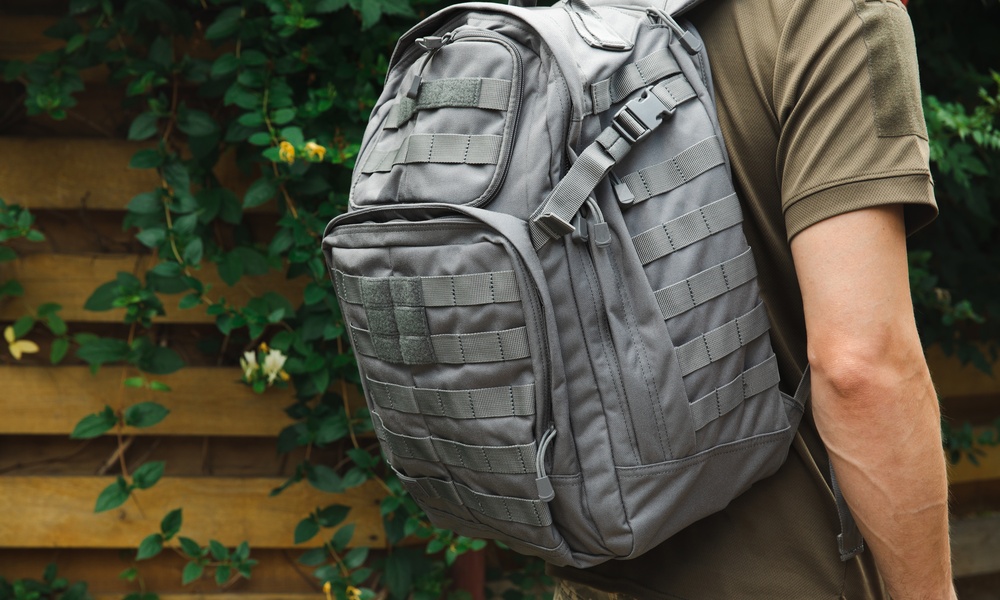 A focus shot of a person wearing a grey MOLLE backpack, a military green t-shirt, and camo pants.