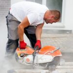 A construction worker uses a stone cutting saw while working on a backyard residential patio project.