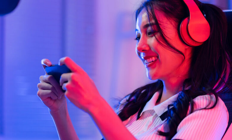 A smiling young person sitting in an office chair, wearing headphones, and holding up a gaming device.