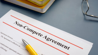 A document with a header reading "Non-Compete Agreement." A yellow pen rests on the paper, and glasses and notebooks sit nearby.