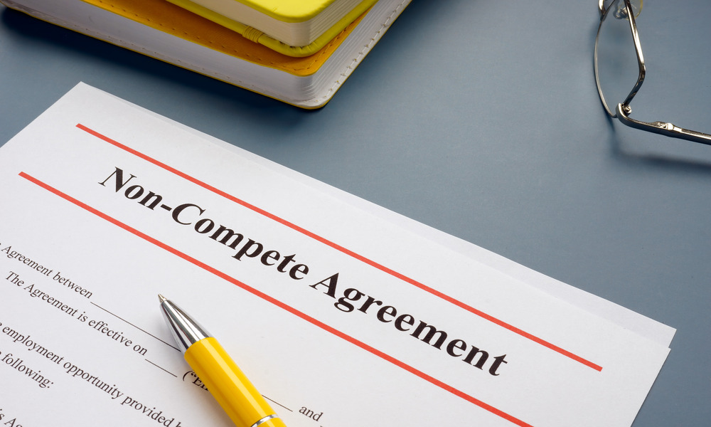 A document with a header reading "Non-Compete Agreement." A yellow pen rests on the paper, and glasses and notebooks sit nearby.