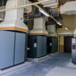 A well-organized facility with four large, gray, industrial air compressor machines with white piping coming out of them.