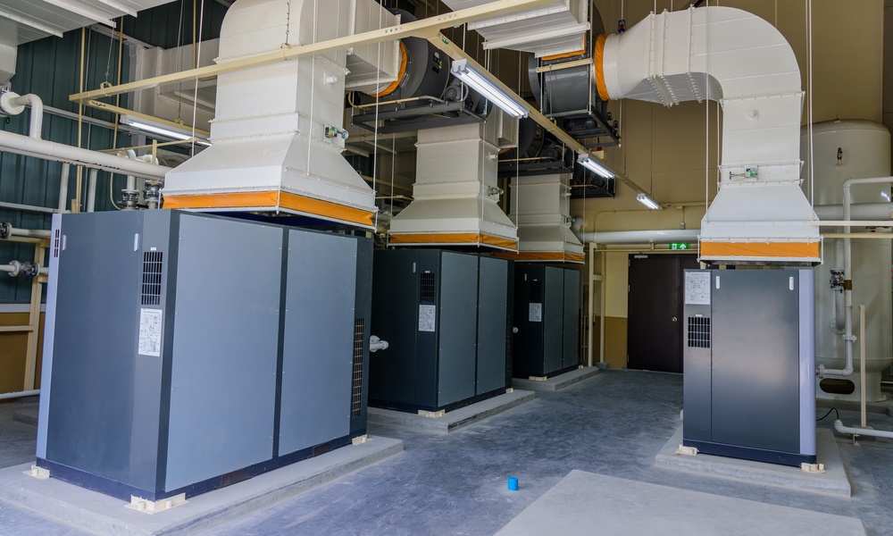 A well-organized facility with four large, gray, industrial air compressor machines with white piping coming out of them.