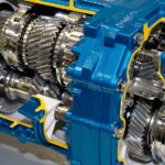 An industrial gearbox that's cut open showing the gears and connections. The gearbox is blue plated with yellow accents.