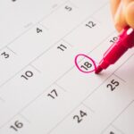 A business professional writing on a calendar with a red marker. They're circling the 18th day on the calendar.