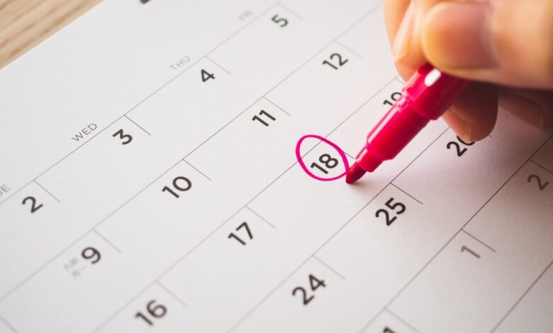 A business professional writing on a calendar with a red marker. They're circling the 18th day on the calendar.