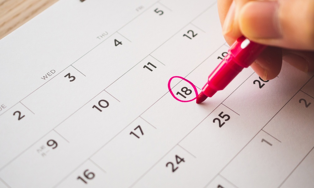 A business professional writing on a calendar with a red marker. They're circling the 18th day on the calendar.