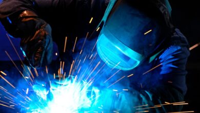 A person wearing a welding mask works on a project, with sparks flying, obscuring the details of the materials.