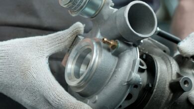 A mechanic wearing soft, white work gloves as he holds a clean turbocharger. The turbocharger is brand new.