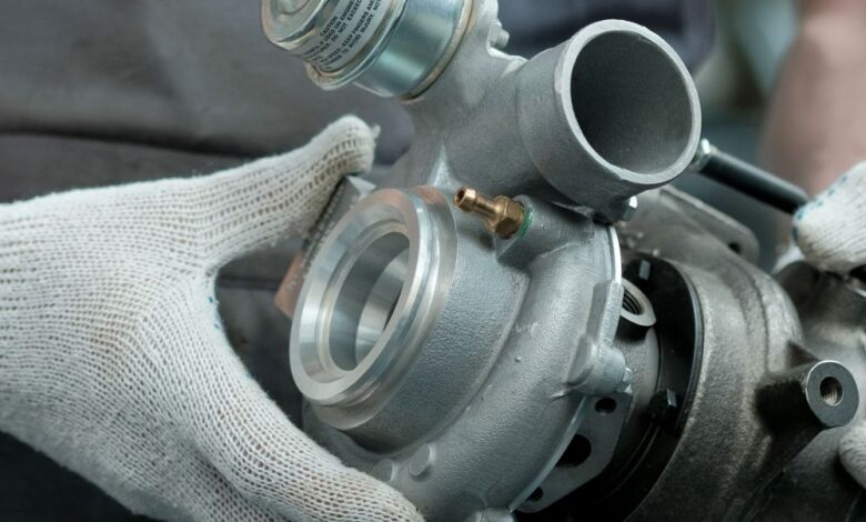 A mechanic wearing soft, white work gloves as he holds a clean turbocharger. The turbocharger is brand new.