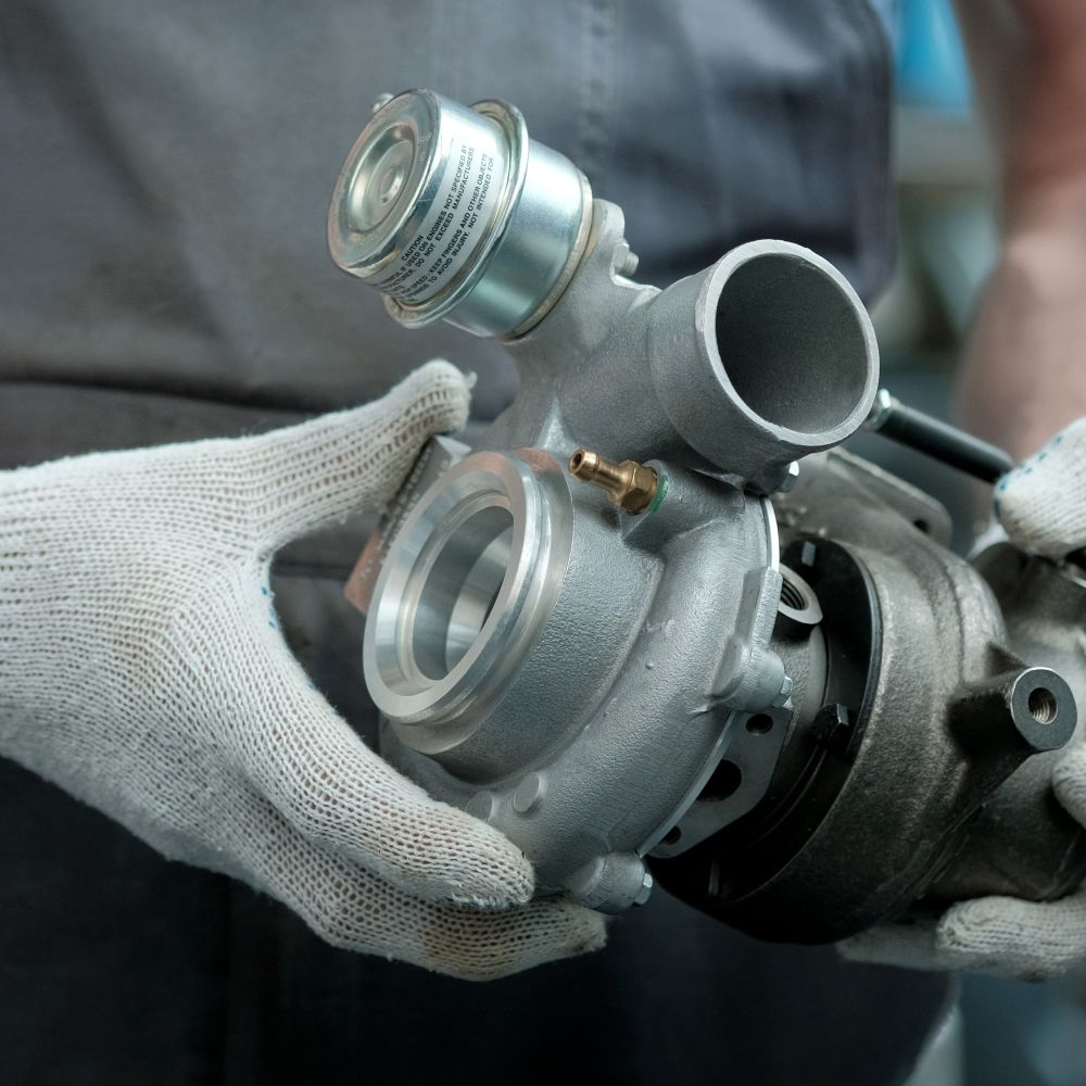 A mechanic wearing soft, white work gloves as he holds a clean turbocharger. The turbocharger is brand new.
