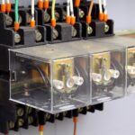 A set of three electrical relays enclosed in glass boxes mounted to a brass rail on a wall, with wires going in and out.