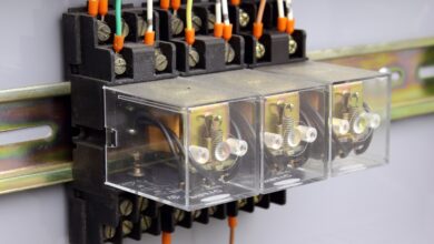 A set of three electrical relays enclosed in glass boxes mounted to a brass rail on a wall, with wires going in and out.
