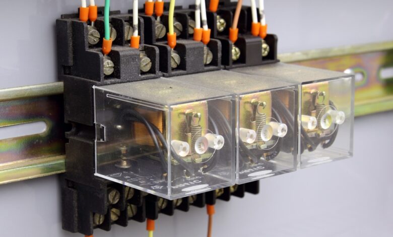 A set of three electrical relays enclosed in glass boxes mounted to a brass rail on a wall, with wires going in and out.