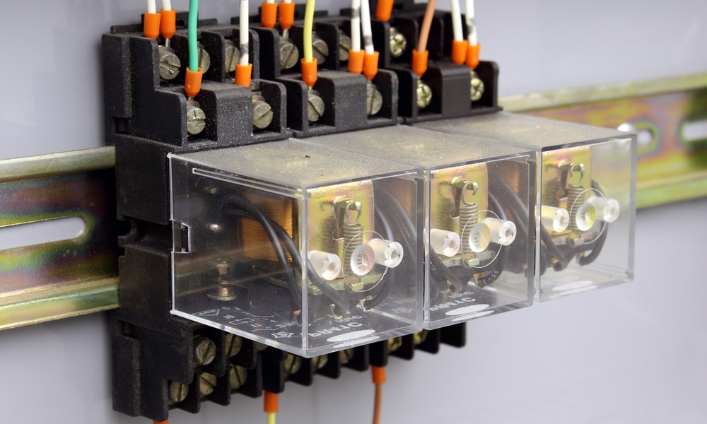 A set of three electrical relays enclosed in glass boxes mounted to a brass rail on a wall, with wires going in and out.