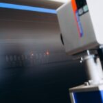 A laser marking machine burning numbers and letters onto the surface of a black water pipe in a factory.