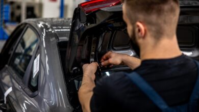 An auto mechanic reworking the tires in a car's trunk lid. The trunk is open and they're working on lighting wires.